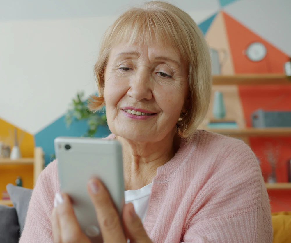 Mujer mayor sonriendo mientras revisa su celular