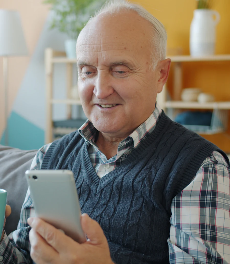 Hombre mayor sonriendo mientras usa su celular en la sala de su casa
